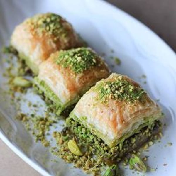Three pieces of baklava, topped with crushed pistachios, on a white rectangular plate.