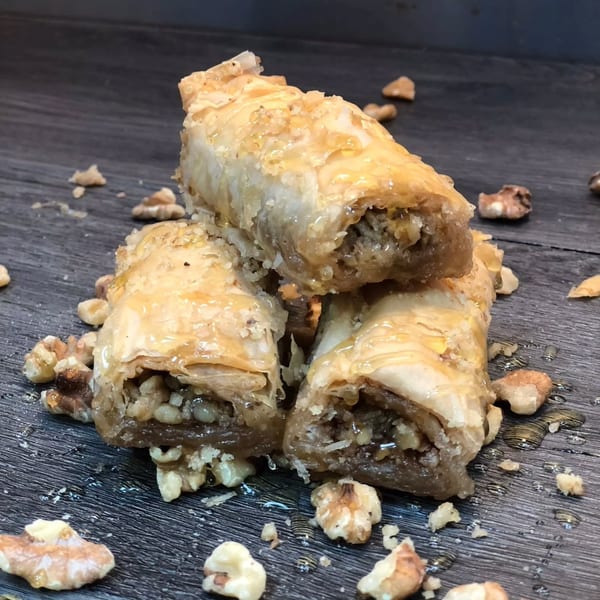Golden, syrup-glazed baklava rolls filled with chopped nuts, stacked on a dark wooden surface.