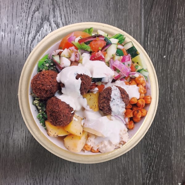 Overhead view of a falafel bowl with salad, chickpeas, potatoes, and white sauce.