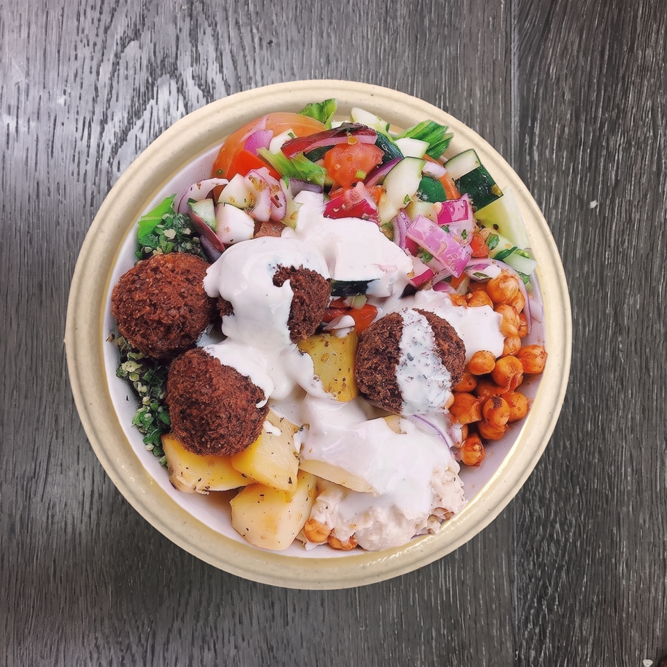 Overhead view of a falafel bowl with salad, chickpeas, potatoes, and white sauce.