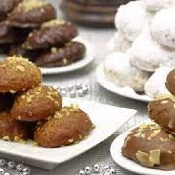 Platters of assorted pastries, including sesame-coated brown sweets and powdered sugar-dusted round treats, arranged on a table.