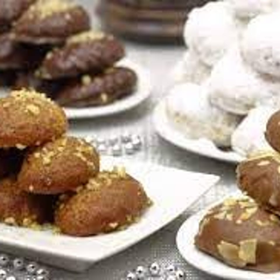 Platters of assorted pastries, including sesame-coated brown sweets and powdered sugar-dusted round treats, arranged on a table.