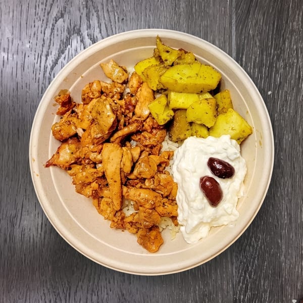 A bowl of chicken, yellow potatoes, and white sauce topped with two olives on a dark wooden surface.