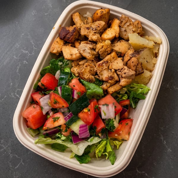 Grilled chicken and potatoes with a fresh salad of lettuce, tomatoes, cucumbers, and red onions.