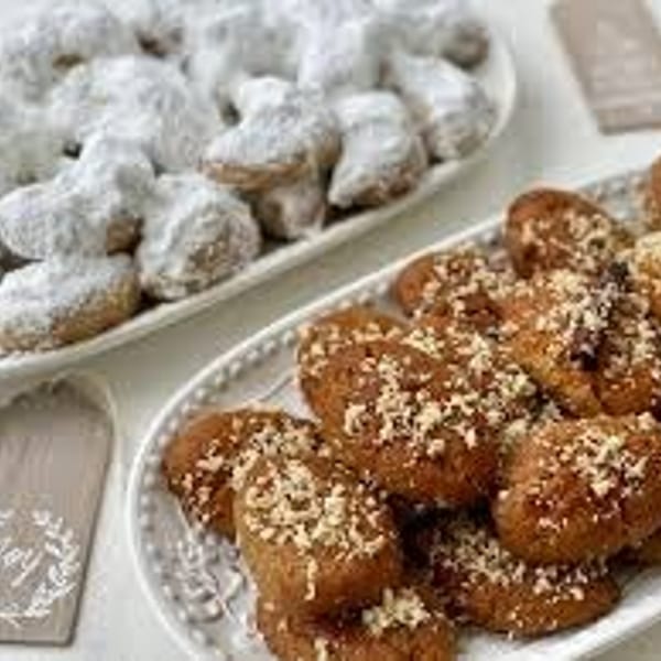 Two white platters of assorted pastries, including powdered sugar-coated pieces and golden pastries sprinkled with sesame seeds.