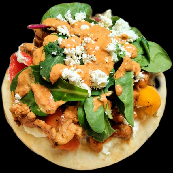 A vibrant chicken gyro with spinach, feta, and a creamy orange sauce on a flatbread.