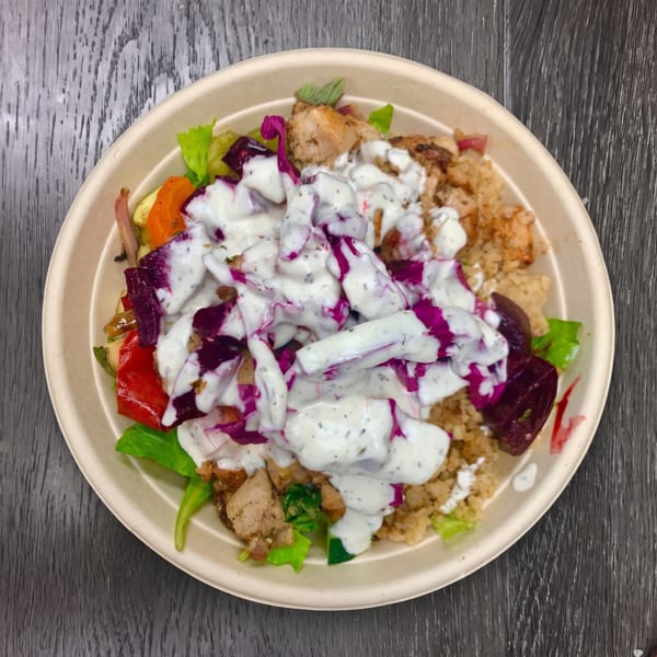 A colorful bowl of chicken, rice, roasted vegetables, and purple cabbage, drizzled with white sauce.