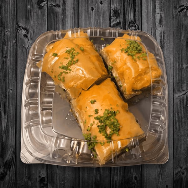 Three golden, herb-topped stuffed pastries arranged in a clear takeout container on a dark wooden table.