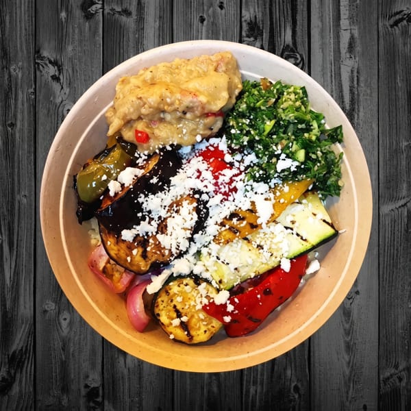 A bowl of grilled vegetables, baba ghanoush, and tabbouleh salad, topped with feta cheese.