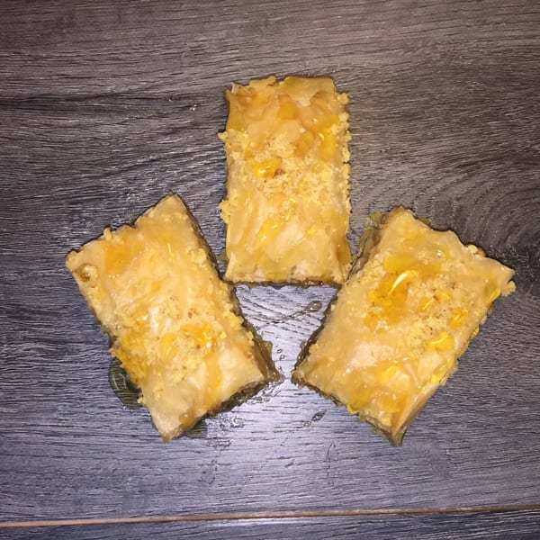 Three golden, syrup-glazed flaky pastries arranged on a dark wood tabletop.