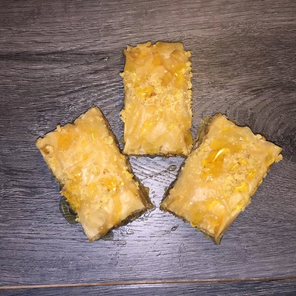 Three golden, syrup-glazed flaky pastries arranged on a dark wood tabletop.